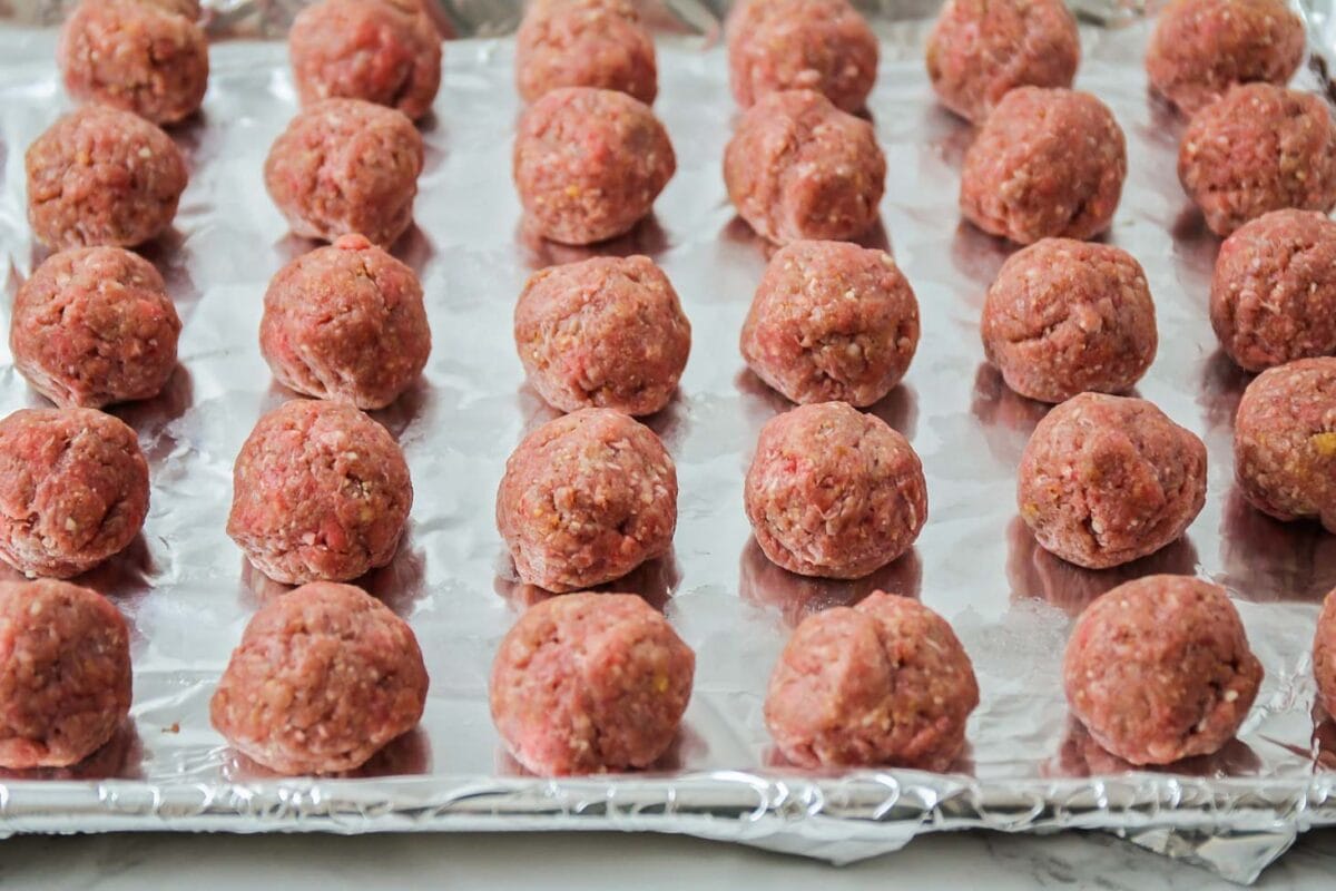 Homemade meatballs lined up on foil lined baking sheet.