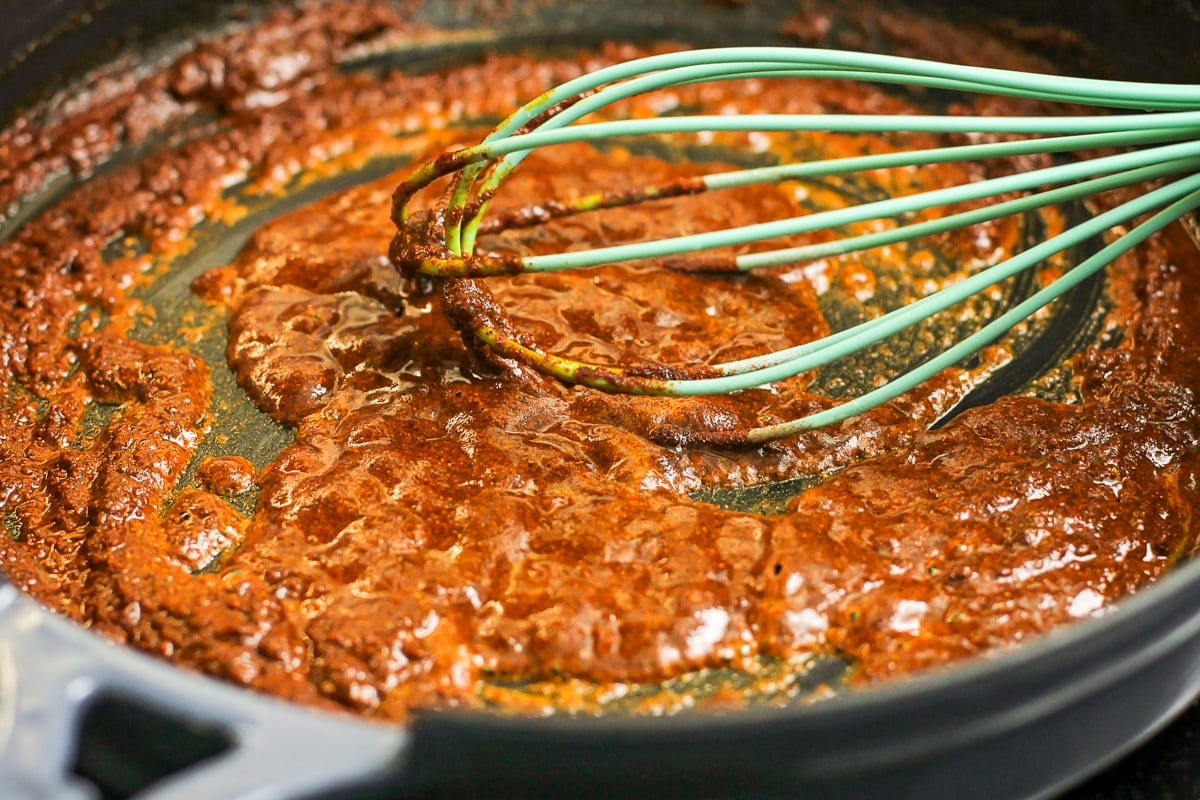 Whisking authentic enchilada sauce in a pan on the stove.