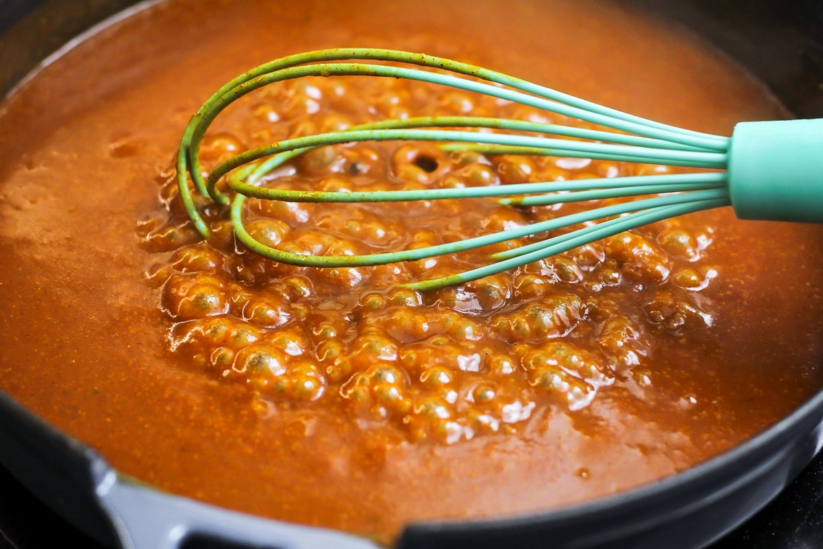 A red enchilada sauce bubbling in a pan on the stove.