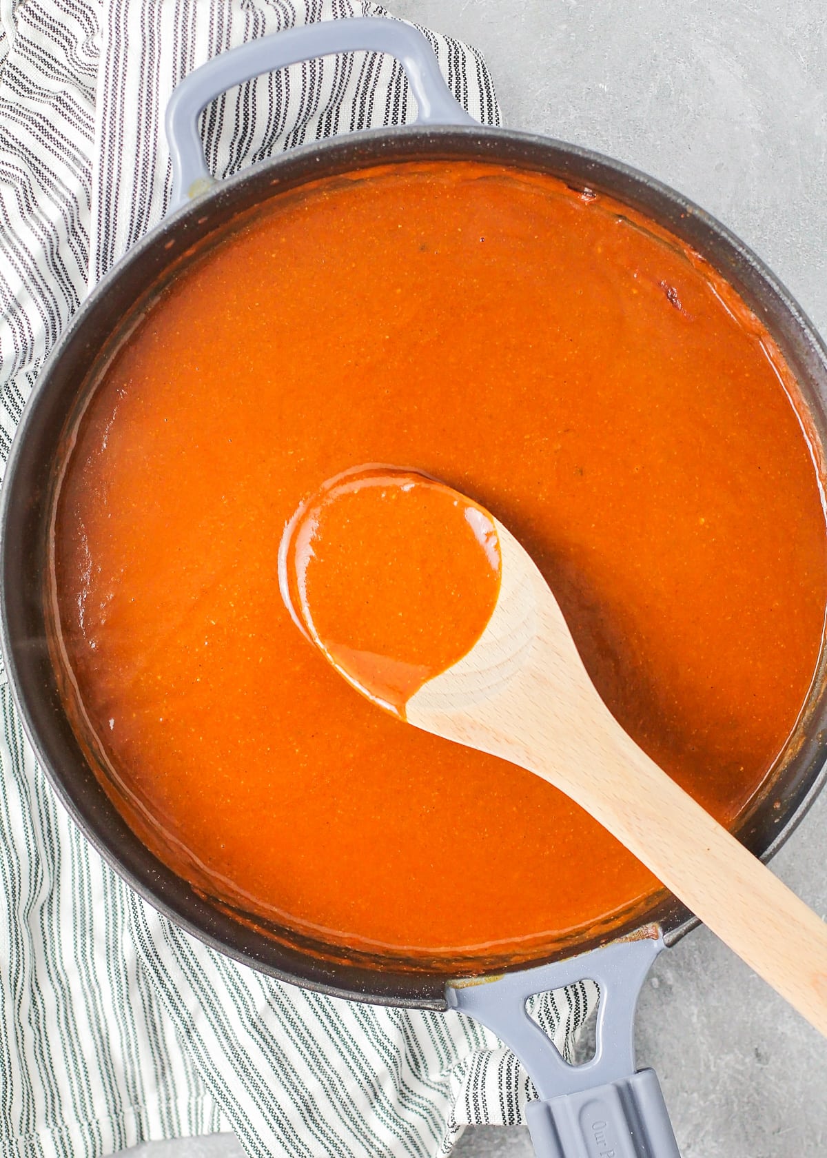 A pot of enchilada sauce with a wooden spoon in the sauce.