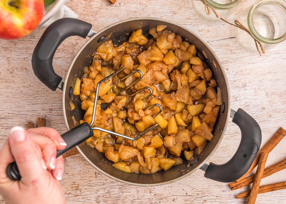 Mashing cooked apples in a pot.