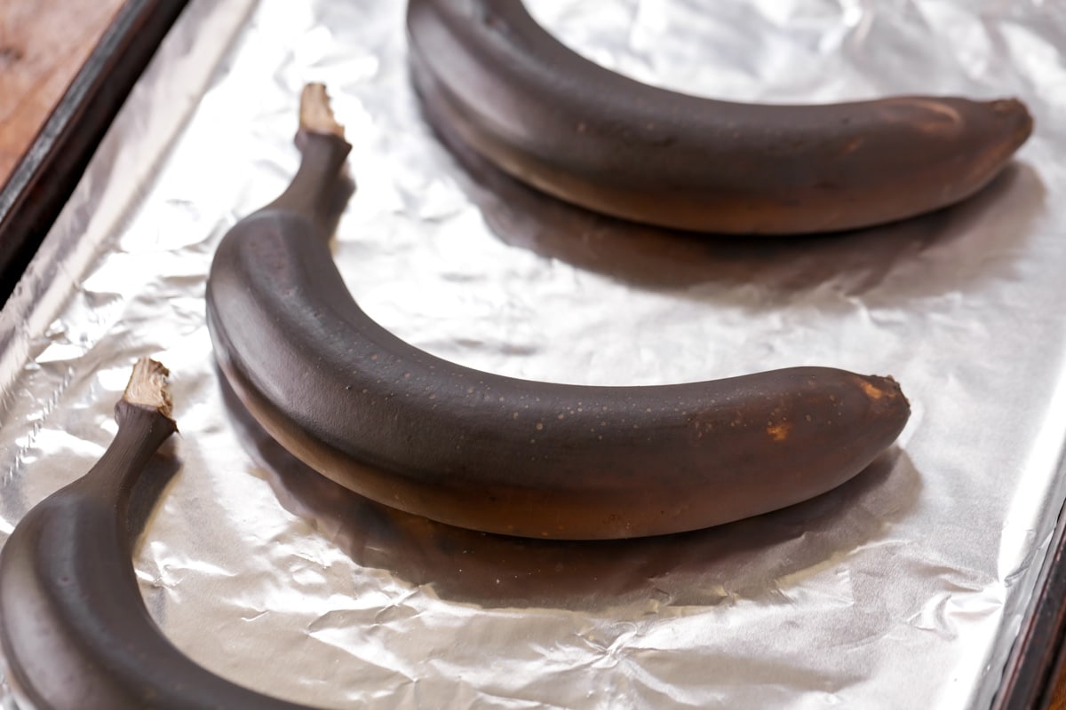 Dark ripened bananas on a lined baking sheet.