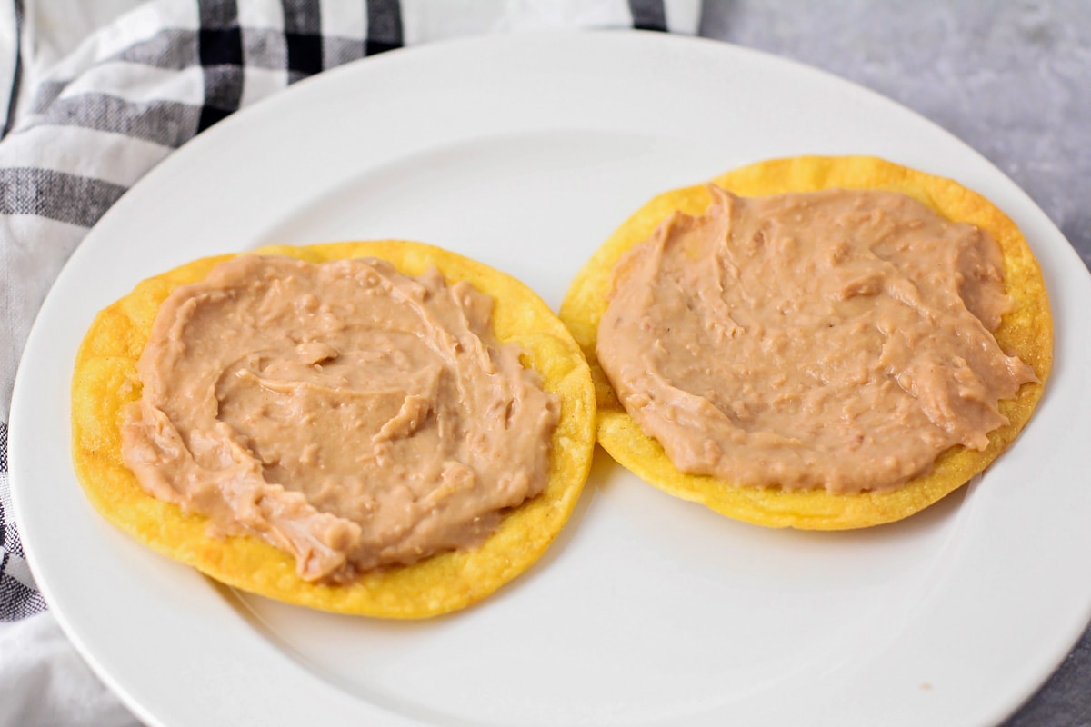 Two fried corn tortillas topped with refried beans.