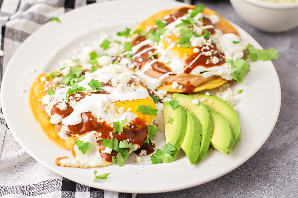 A plate of huevos rancheros topped with crema and cotija cheese with a sprinkling of cilantro.