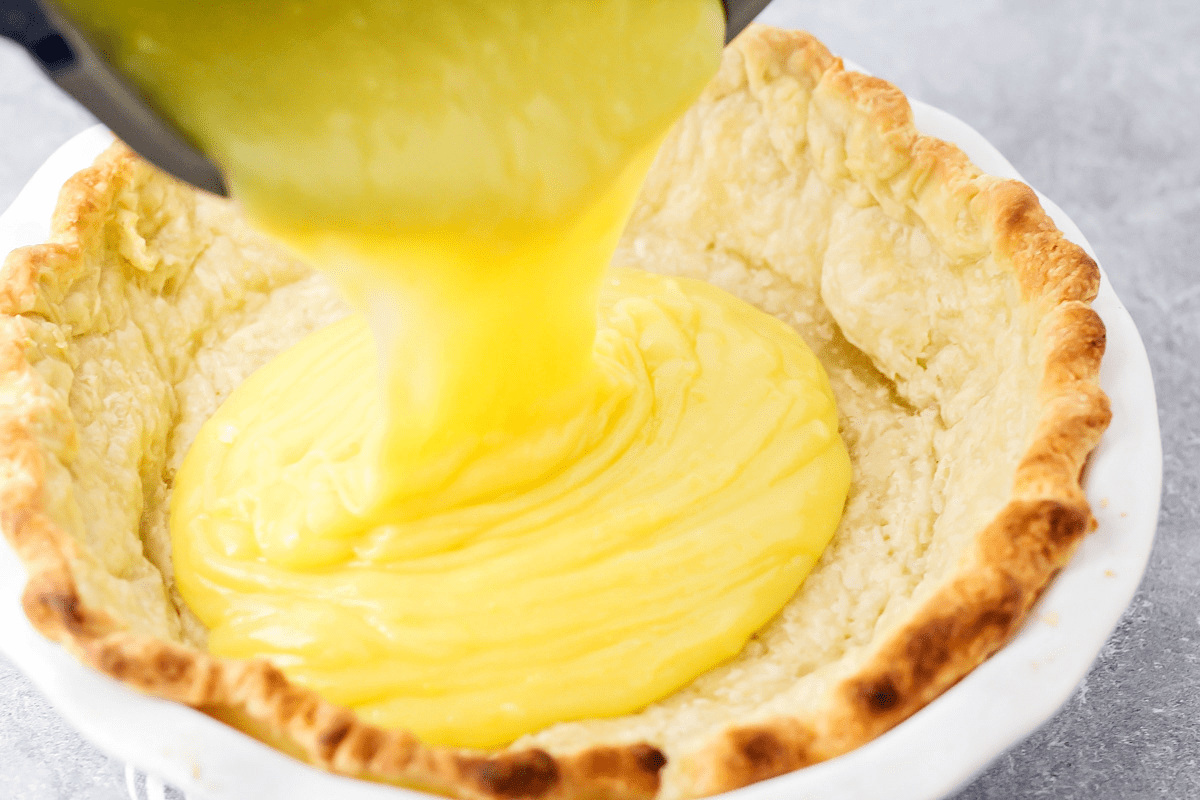Pouring lemon filling into a blind baked pie crust.