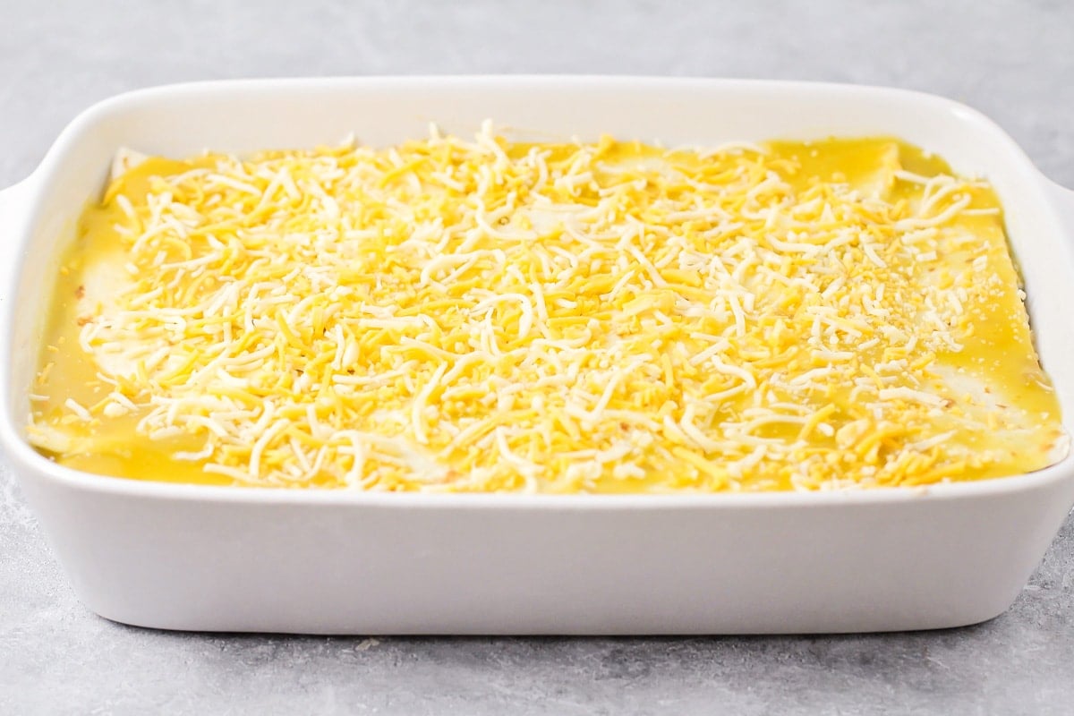Topping the casserole with enchilada sauce and shredded cheese.