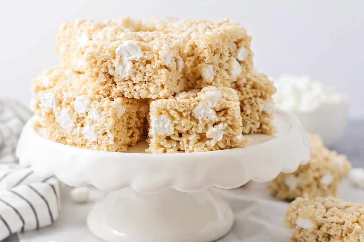 Rice krispie treats cut and stacked with on a white cake platter.