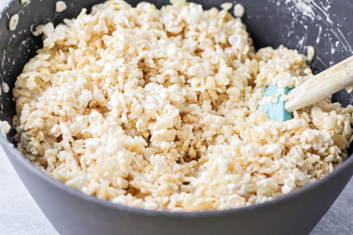 Combining rice krispies, melted butter, and marshmallows.