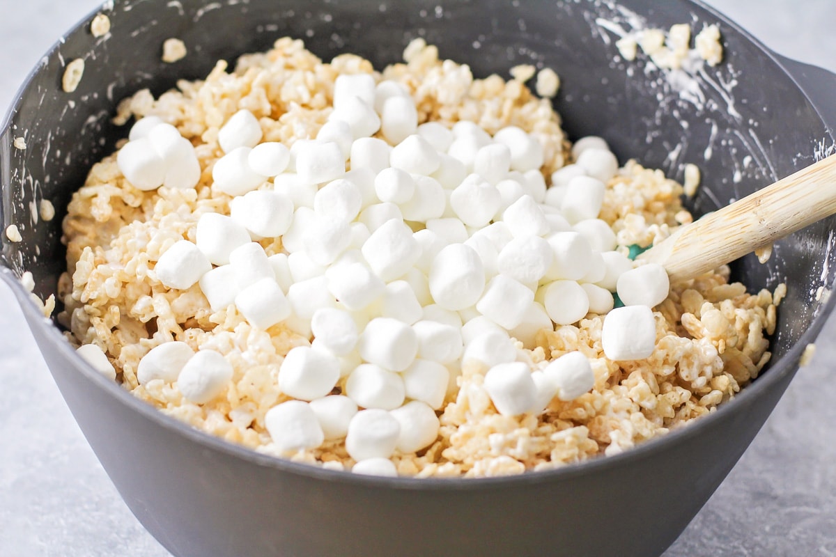 Adding mini marshmallows to a mixture of rice krispies.