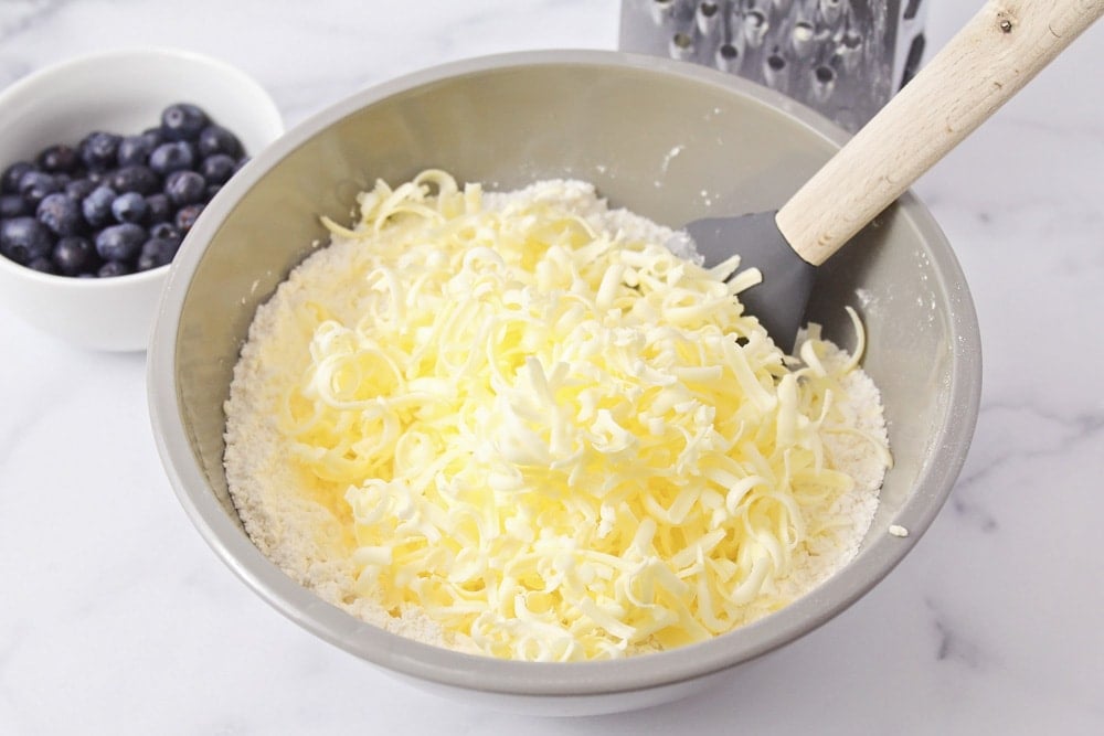 Adding grated butter to dry ingredients in a mixing bowl.