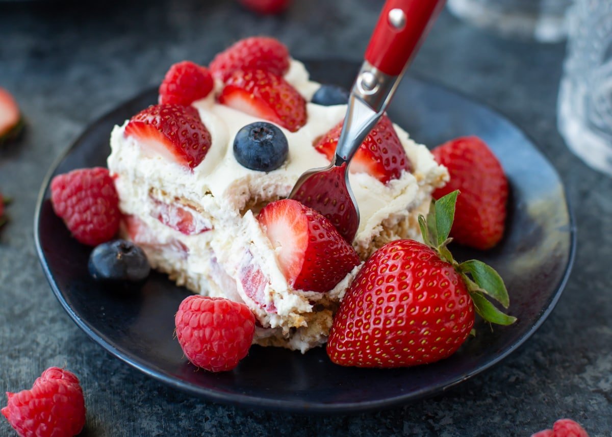 A slice of strawberry ice box cake topped with fresh berries.