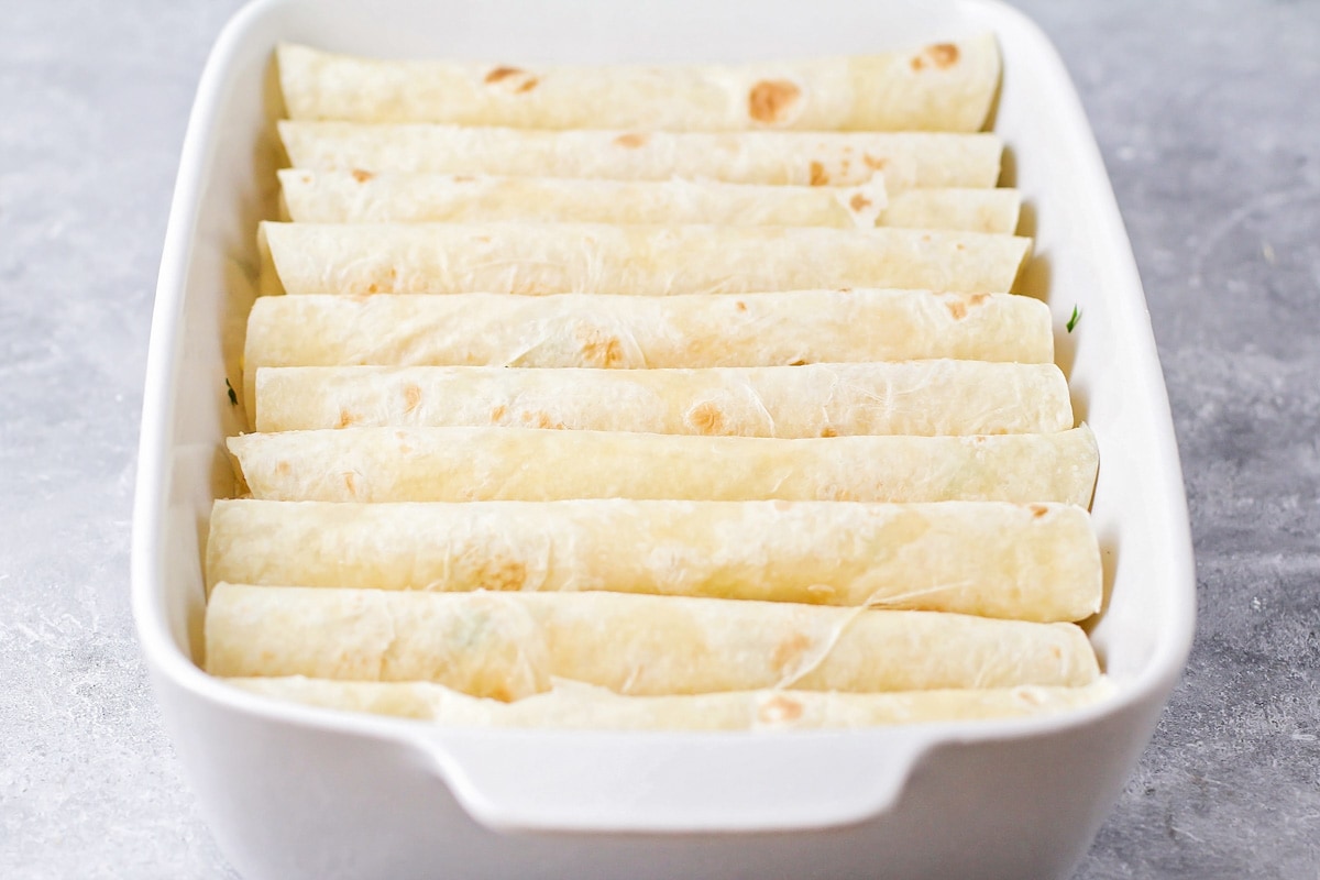 Rolled tortillas filled with chicken in a white baking dish.