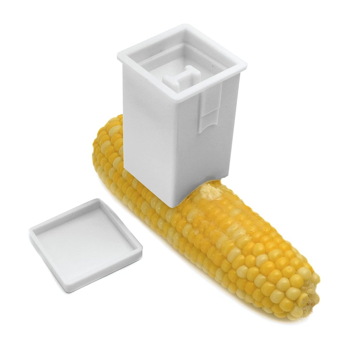 A rectangular white tool with an arched edge buttering a piece of corn on the cob.