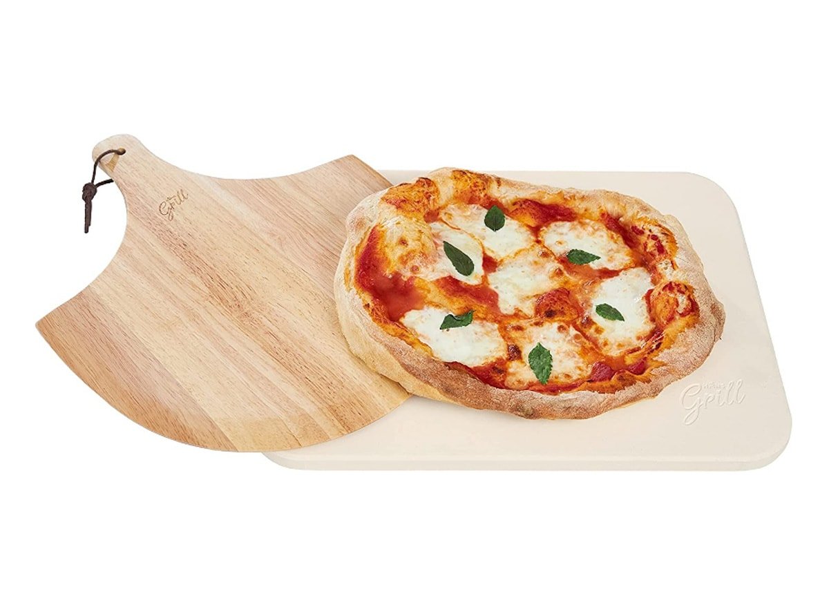 A pizza on a beige rectangular pizza stone and a wooden board used to move the pizza.
