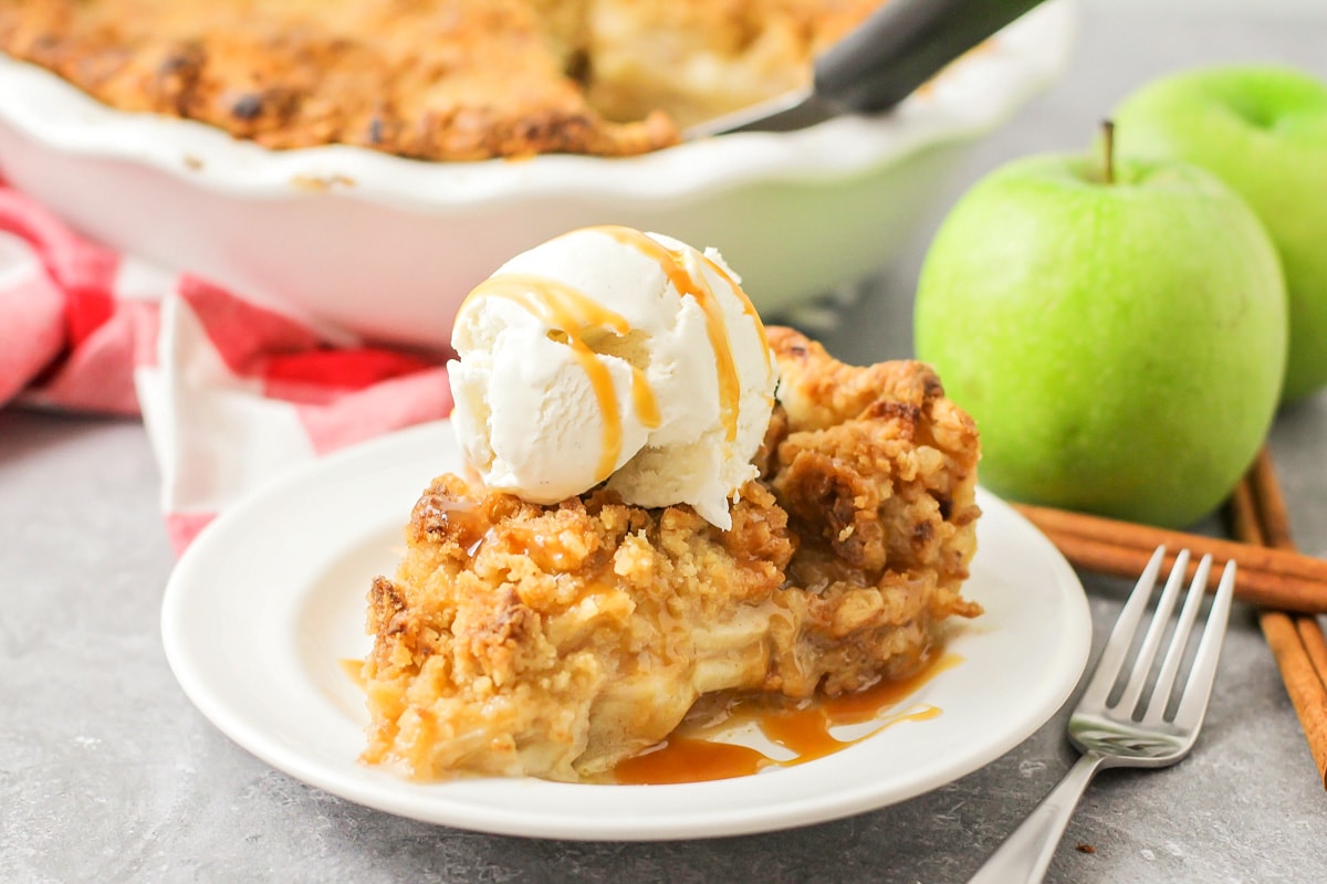 A slice of apple crumble pie topped with vanilla ice cream and caramel.