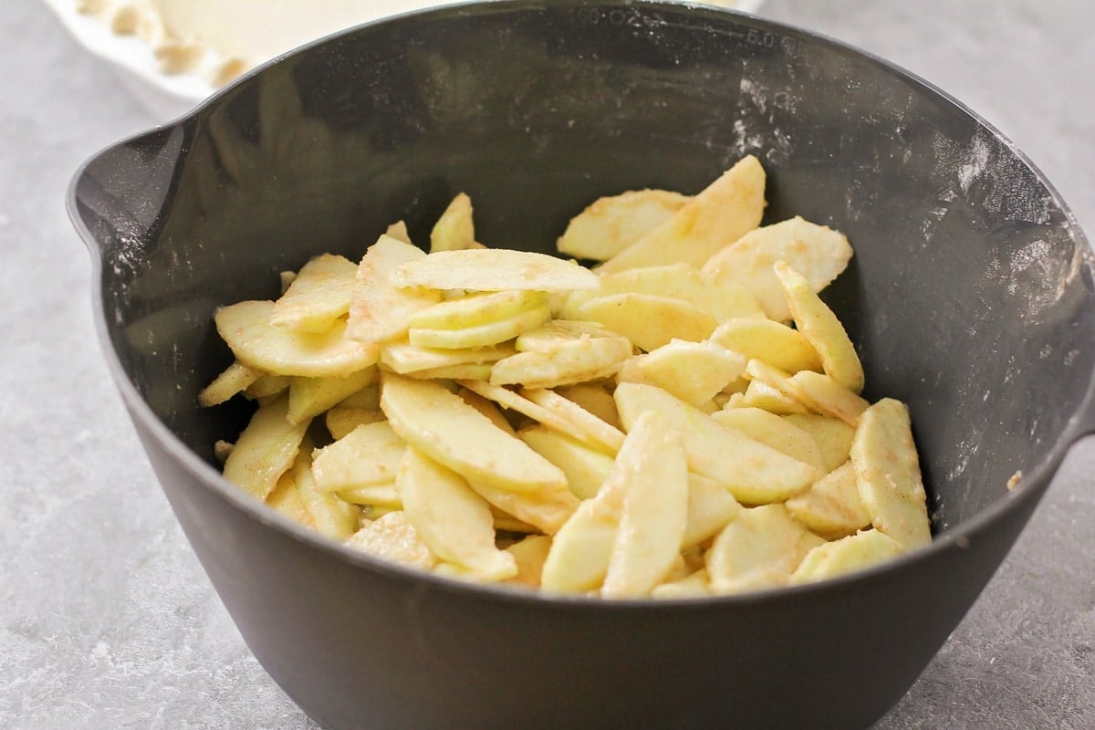 Mixing sliced apples and brown sugar in a grey bowl.