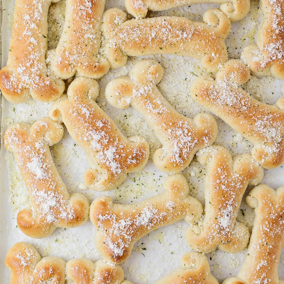 Several breadsticks on a baking sheet sprinkled with parmesan cheese.