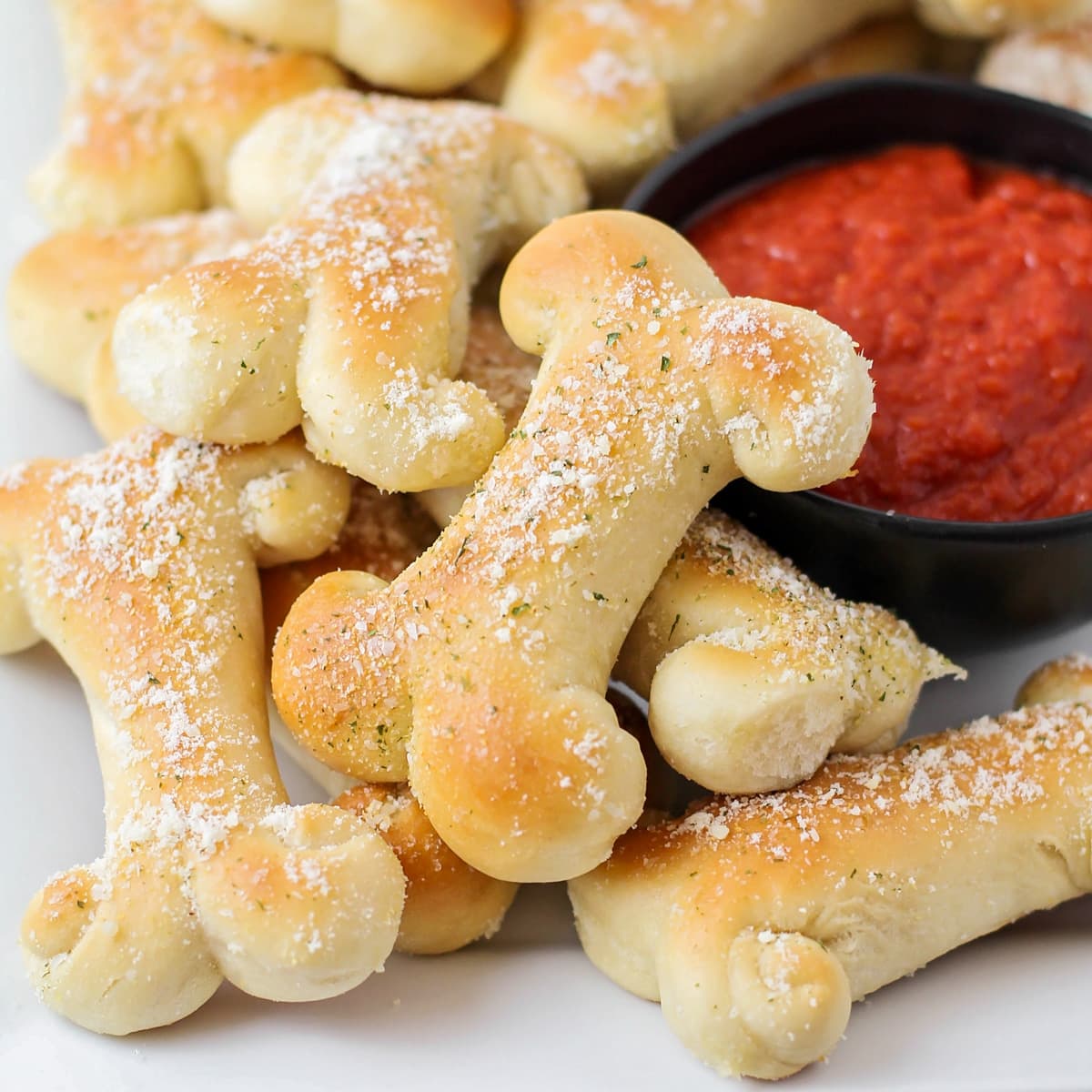 A pile of cheesy breadstick bones served with a bowl of marinara.