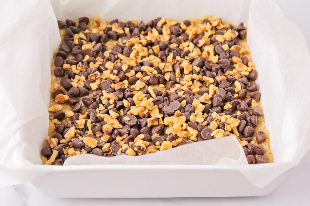 Chocolate chips spread over oat base in baking pan.