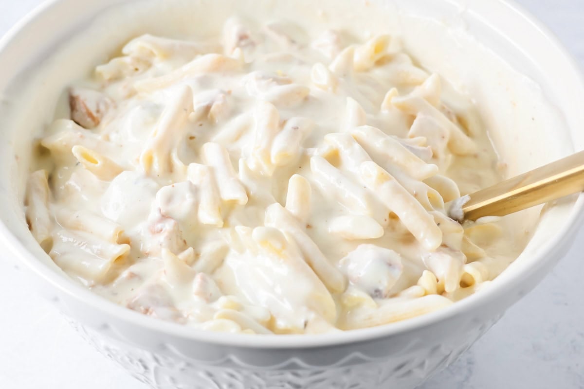 Mixing pasta and sauce in a bowl for chicken alfredo bake.
