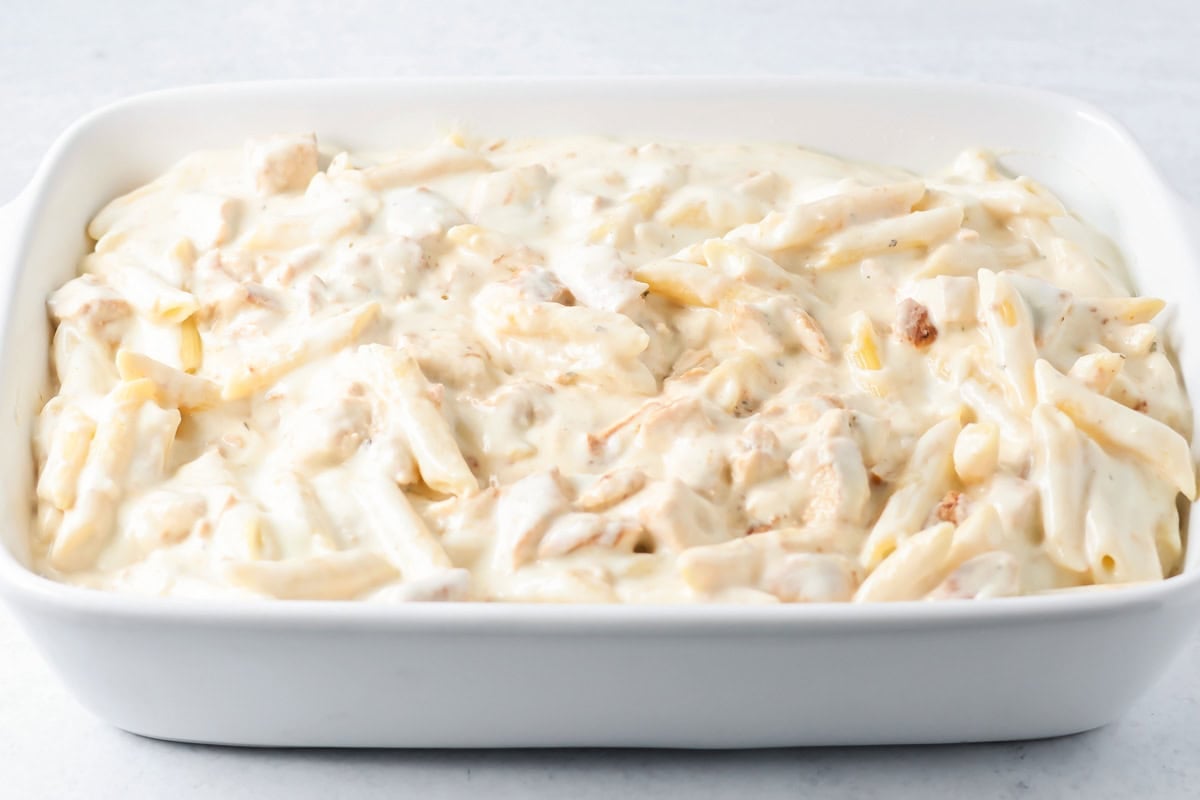 Pasta mixture poured in a baking dish for chicken alfredo bake.