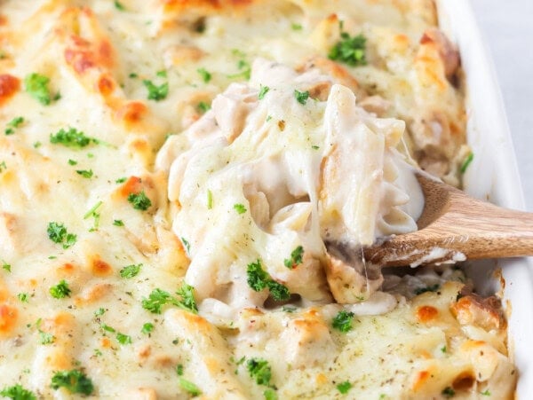 Scooping chicken alfredo bake from a pan.