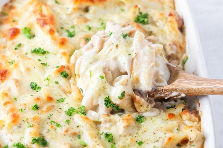 Scooping chicken alfredo bake from a pan.