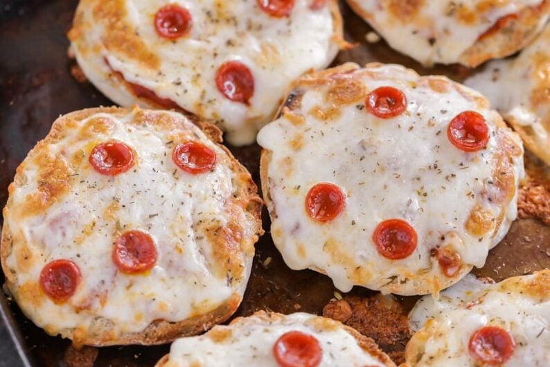 Mini pizzas made out of English muffins with tiny pieces of pepperoni on them.