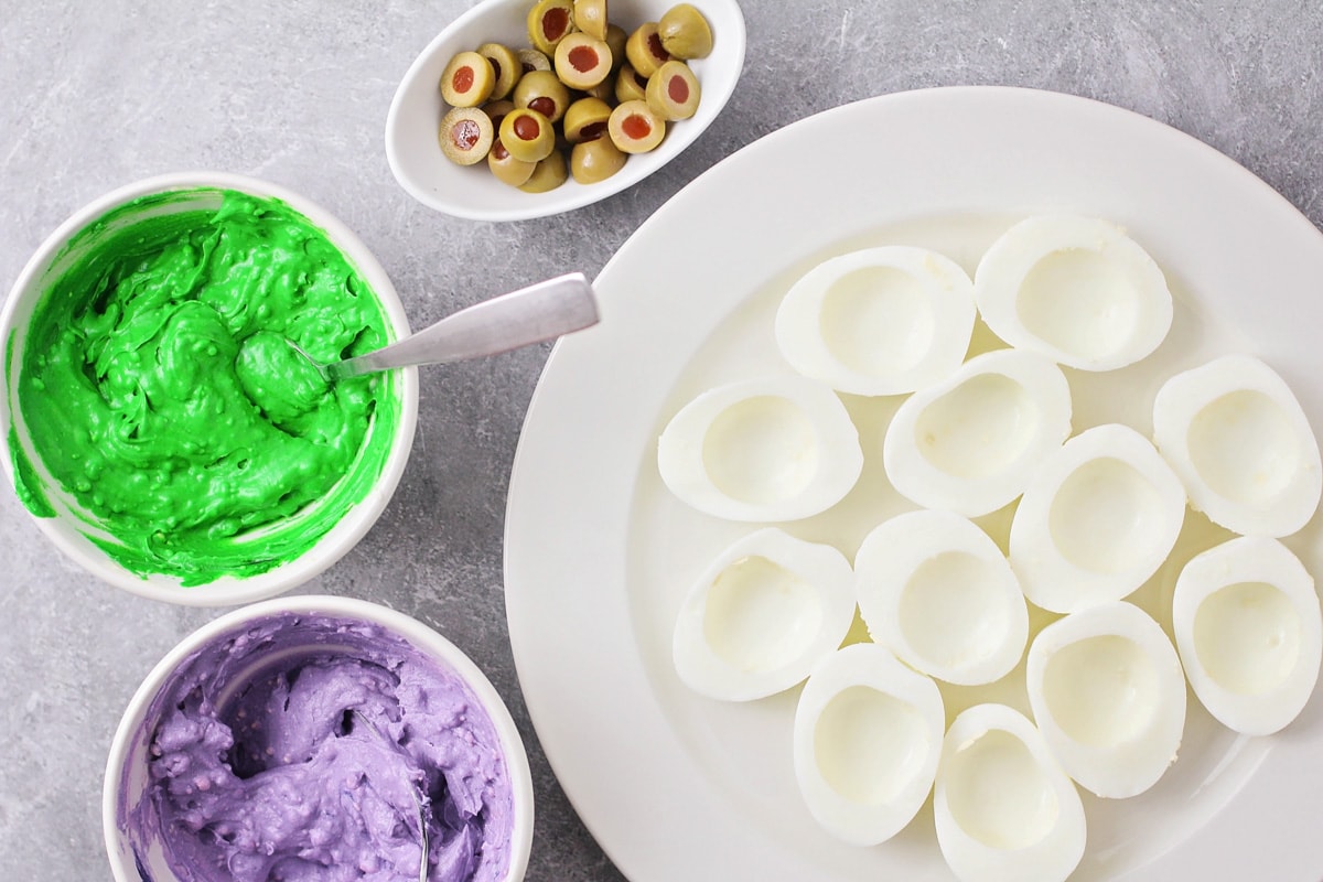 Prepping to fill deviled eggs with green and purple filling.