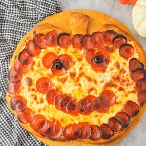 Halloween pizza with pepperoni and olive shaped like a jack o'lantern.