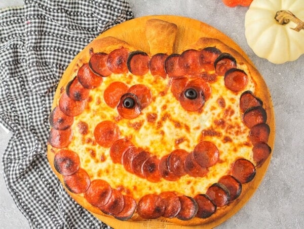 Halloween pizza with pepperoni and olive shaped like a jack o'lantern.