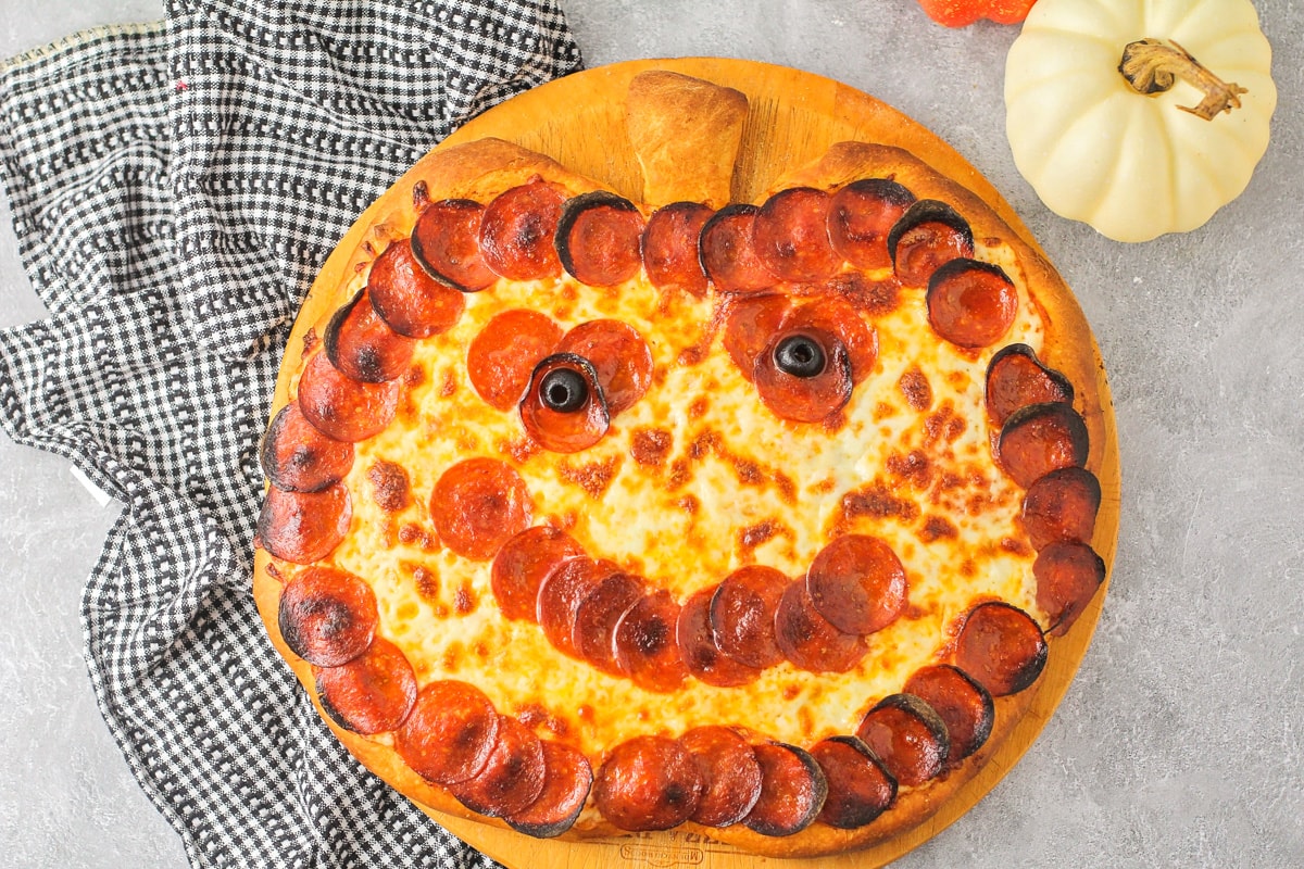 A halloween pizza shaped like a jack o lantern with olive eyes.