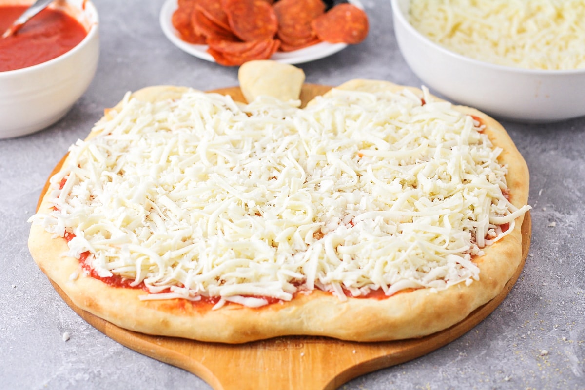 Adding cheese to a pumpkin shaped pizza.