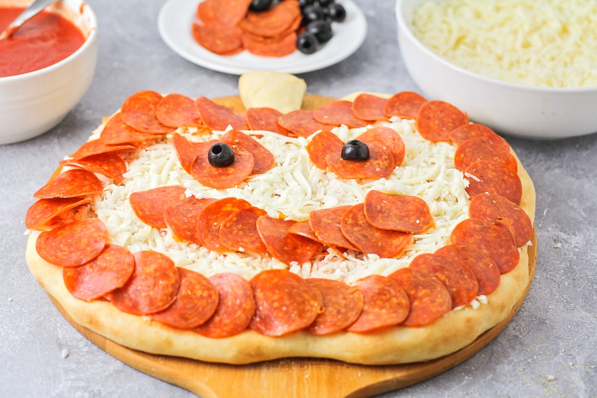 Olive eyes and pepperoni outlining a pumpkin shaped pizza.