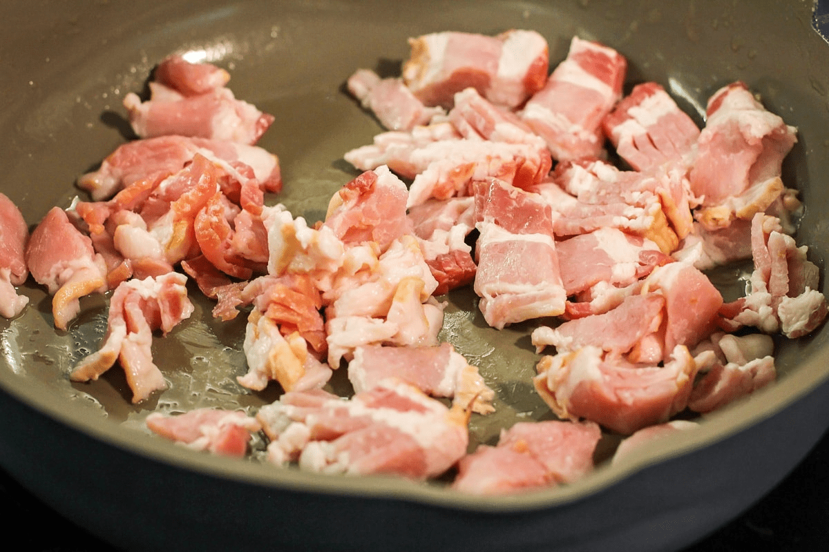 Chopped pieces of bacon cooking in a pan.