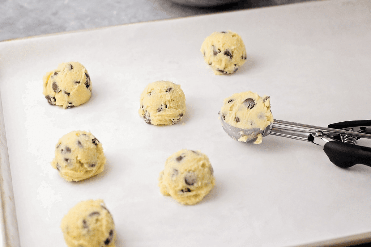Scooping cookie dough onto parchment paper with an ice cream scoop.