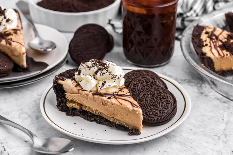 A slice of mud pie served on a white plate with Oreo cookies and topped with whipped cream.