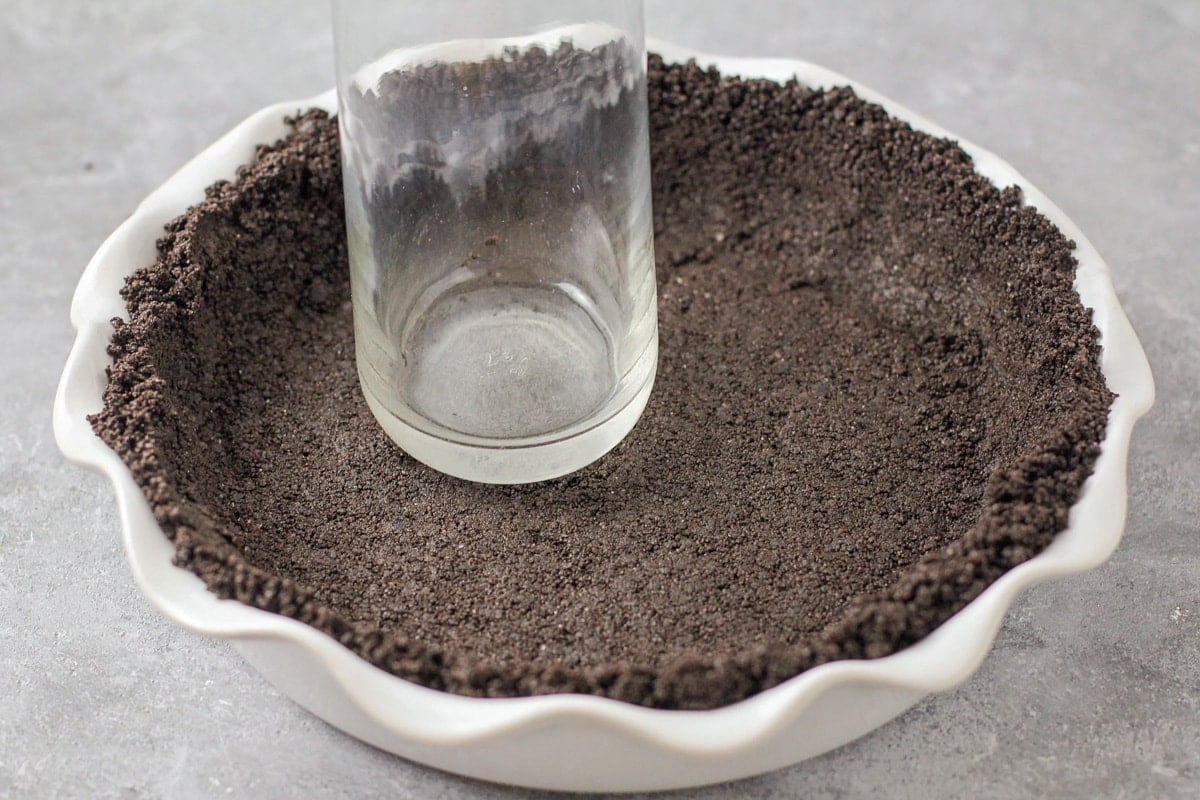 Pressing oreo crumbs in a pie pan with a glass.