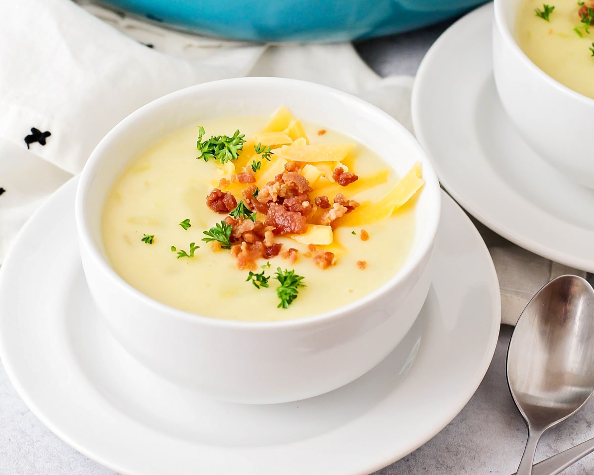 Potato leek soup served in a white bowl and topped with bacon bits and cheese.