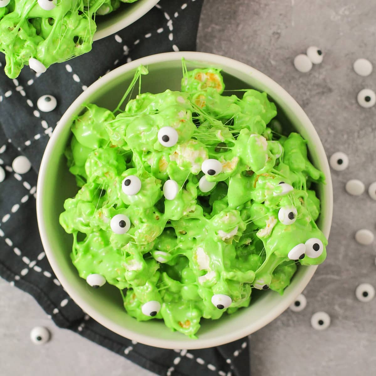A white bowl filled with green slime popcorn with candy eyeballs.