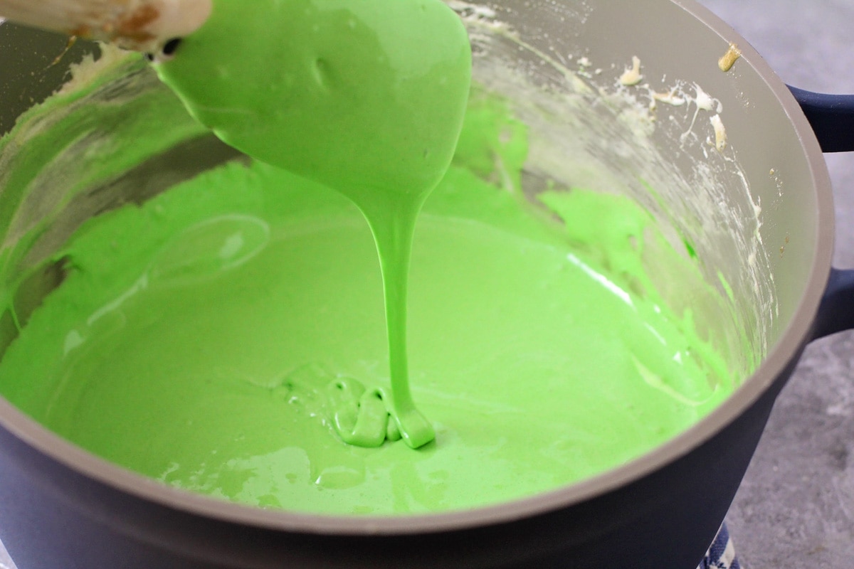 Adding green food coloring to the marshmallow caramel mixture.