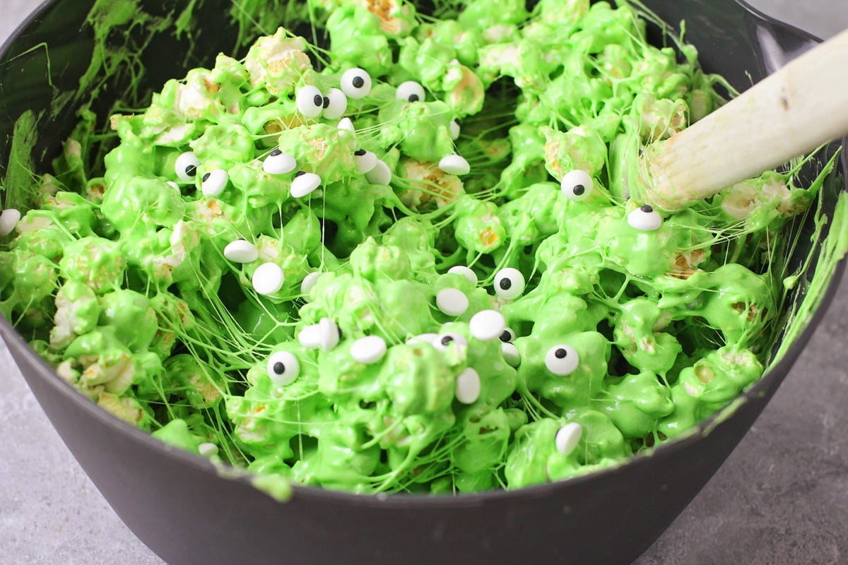 Mixing the green marshmallow mixture with the popcorn and candy eyeballs.