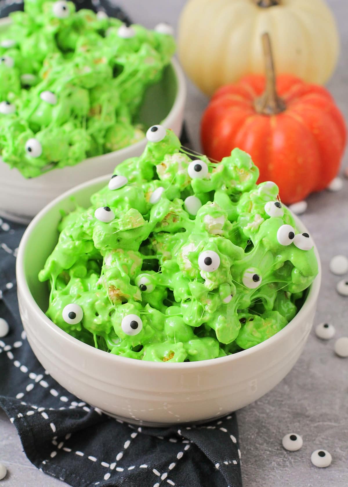 A white bowl filled with green slime popcorn covered in candy eyeballs.