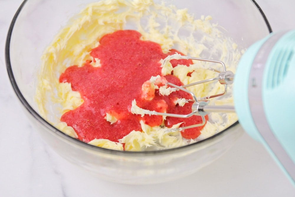 How to make strawberry frosting process pictures - ingredients being mixed with an electric mixer in a clear glass bowl. 