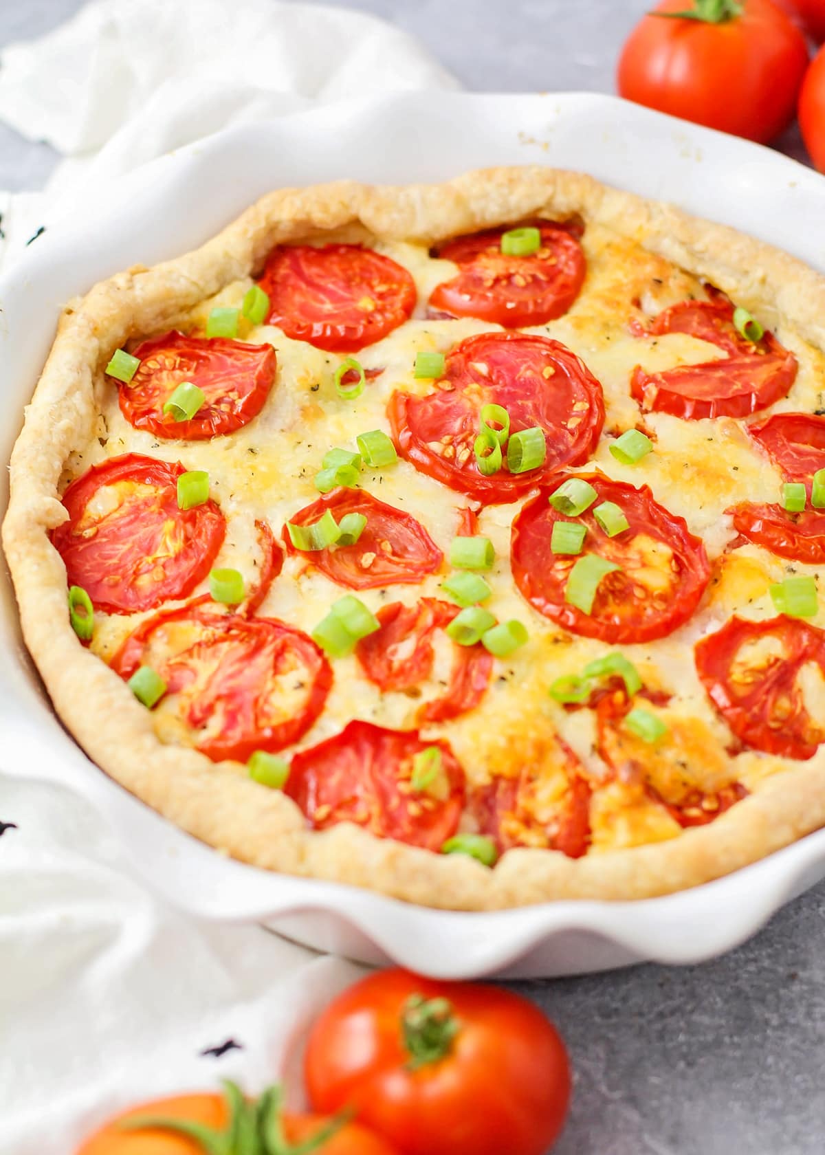 A whole tomato pie topped with green onions and served in a white pie dish.