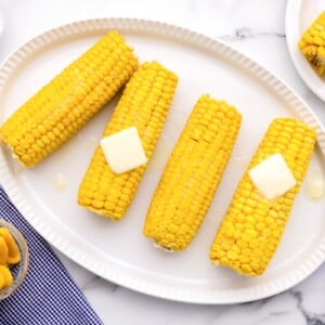 How to boil corn on the cob tutorial with cobs served on a white platter and topped with butter.