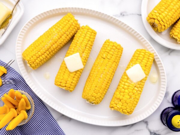 How to boil corn on the cob tutorial with cobs served on a white platter and topped with butter.