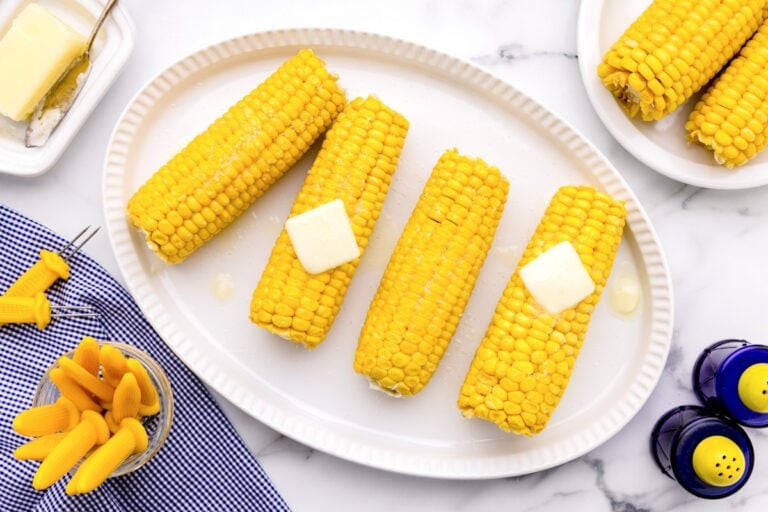 How to boil corn on the cob tutorial with cobs served on a white platter and topped with butter.