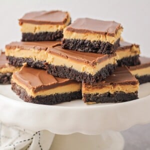 Several buckeye brownies stacked on a white cake platter.