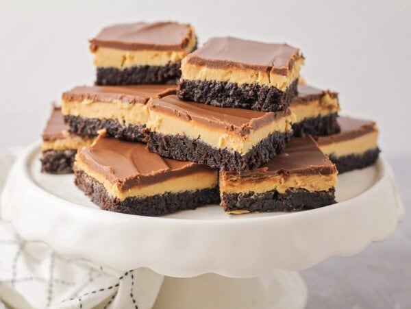 Several buckeye brownies stacked on a white cake platter.